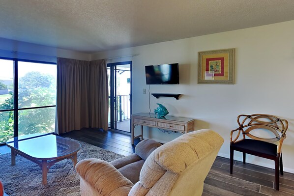 A living room with a sofa, armchair, coffee table, TV, and a framed picture on the wall.