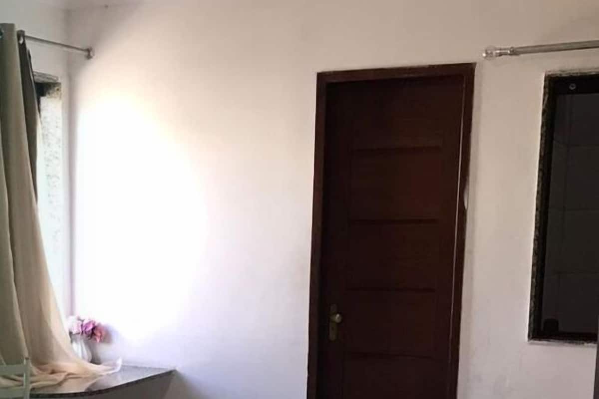 Una habitación pequeña y sencilla con dos camas, una puerta de madera y una ventana con cortina.