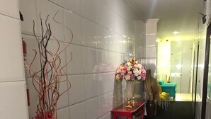 Un passadís amb parets de rajola blanca, una tauleta de consola vermella amb un ram de flors roses, i una planta decorativa amb flors roses.