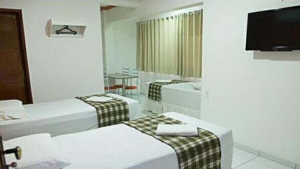 Habitació d'hotel amb dos llits, una taula petita, una cadira, televisió i finestra amb cortines.