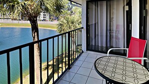 Un balcon avec vue sur une étendue d’eau, un palmier et une table avec une chaise.