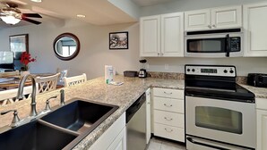 A kitchen with white cabinets, a granite countertop, a sink, a stove, an oven, a microwave, and a ceiling fan. - Edgewater Villa #2209 | Lake View, Beach Tram + Resort Amenities (Panama City Beach)