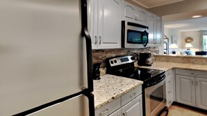 A modern kitchen with white cabinets, a stainless steel refrigerator, a microwave, and a stove. - Edgewater Villa #2301 | Golf, Beach, 11 Pools! (Panama City Beach)