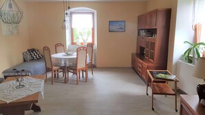 A cozy living room with a dining area, a sofa, a wooden cabinet, and a small table with a lamp. - Idyllic vacation apartment on the farm  (Baruth)