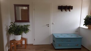 A room with a wooden door, a small wooden stool with a potted plant, a blue chest of drawers with floral designs, and a wall-mounted coat rack with shoes. - Idyllic vacation apartment on the farm  (Baruth)