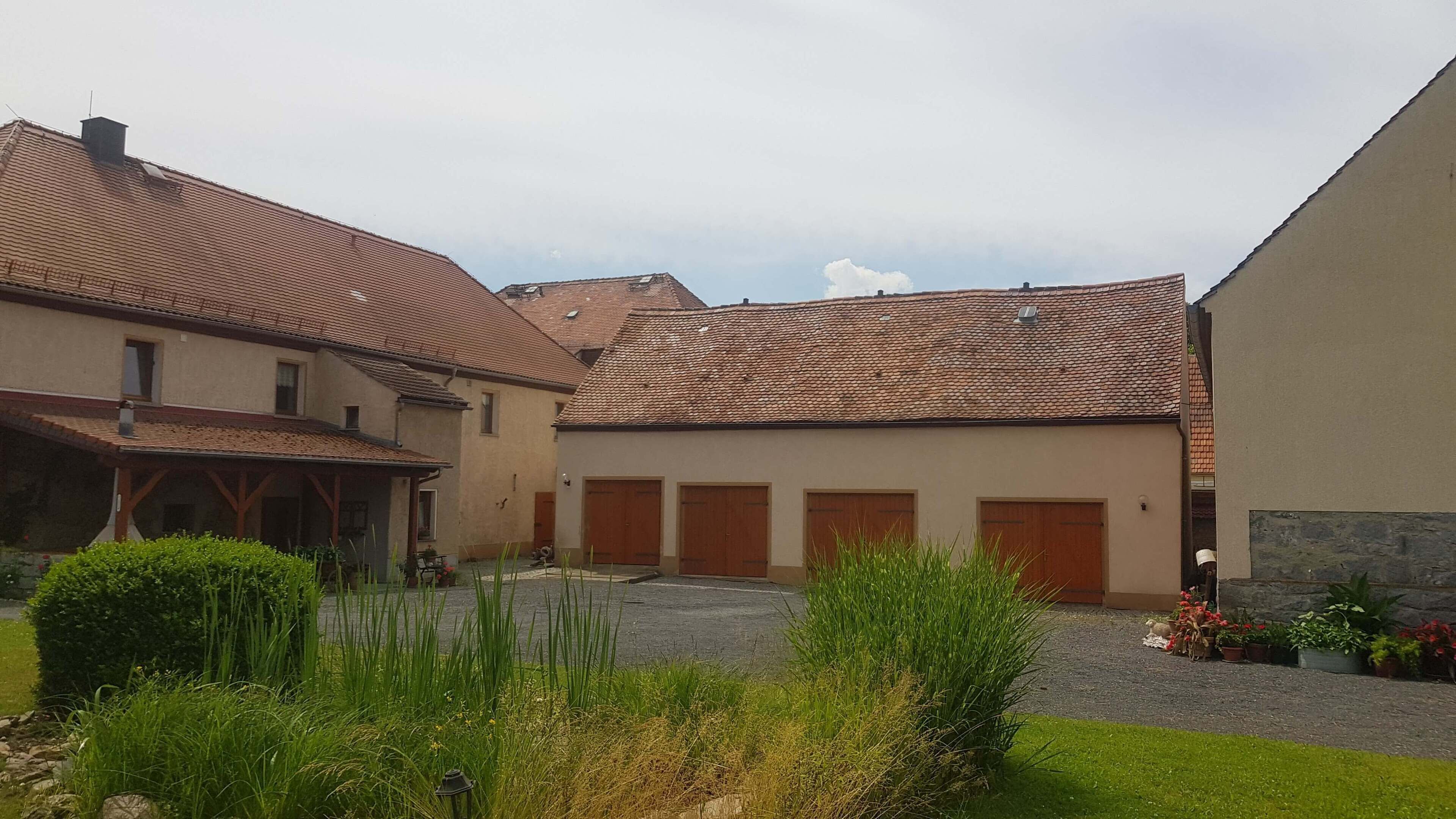 Un cortile con edifici, una zona salotto coperta e un vialetto sterrato.