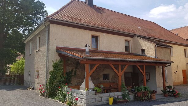 A two-story house with a tiled roof, a covered porch with wooden beams, and a stone foundation. - Idyllic vacation apartment on the farm  (Baruth)