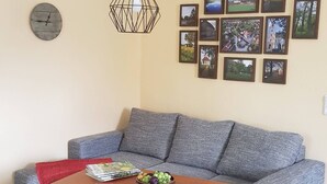 A living room with a grey sofa, a wooden coffee table, a red throw, and a wall clock. - Idyllic vacation apartment on the farm  (Baruth)
