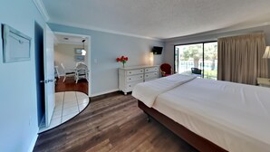 Habitación de hotel con una cama grande, un escritorio con silla, un tocador con espejo y una ventana con cortinas.