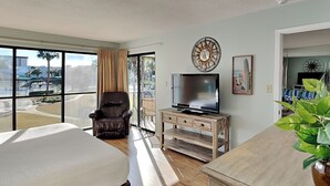 Une chambre d’hôtel avec un grand lit, un téléviseur posé sur un meuble en bois, une chaise et une vue sur l’extérieur grâce à de grandes fenêtres.
