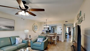 A modern living room with a ceiling fan, a dining area with a chandelier, and a kitchen in the background.