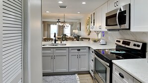 A modern kitchen with white cabinets, a built-in oven, a microwave, and a dining area with a chandelier.