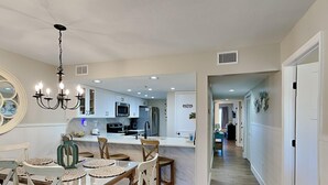 A modern kitchen with white cabinetry, a central island, and a dining area with a wooden table and chairs.