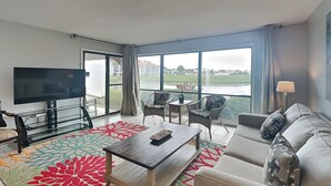 Una habitación de hotel moderna con un ventanal grande, un televisor de pantalla plana, un sofá, una mesa de centro y una pequeña mesa con sillas.