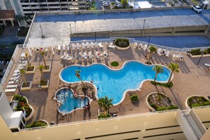 A rooftop pool area with multiple swimming pools, sun loungers, and palm trees.