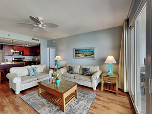 A living room with a sofa set, a coffee table, two lamps, a ceiling fan, and a painting on the wall.