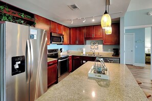 A modern kitchen with stainless steel appliances, wooden cabinets, granite countertops, and a pendant light.