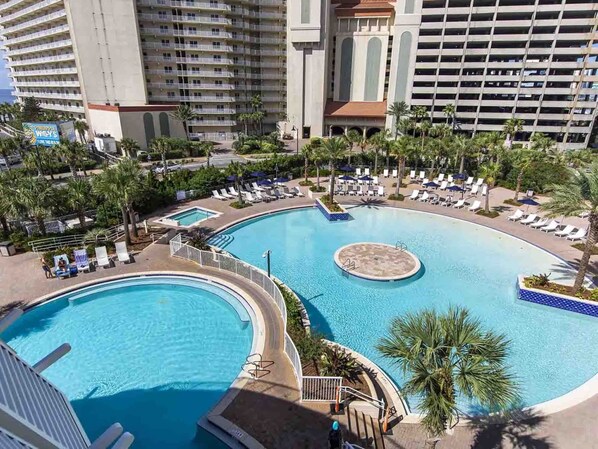 A resort with a large pool area, palm trees, and multiple buildings in the background.