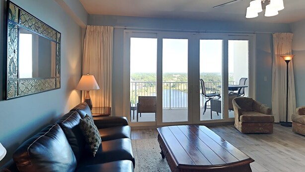 A living room with a leather sofa, a wooden coffee table, and a view of a balcony with outdoor furniture. - Laketown Wharf #1337 | Waterfront Paradise! (Panama City Beach)