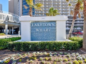 A sign for Lake Town Wharf with a modern building in the background.