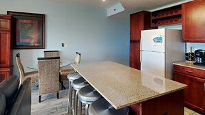 A kitchen with a granite countertop, bar stools, a refrigerator, and wooden cabinets. - Laketown Wharf #1337 | Waterfront Paradise! (Panama City Beach)