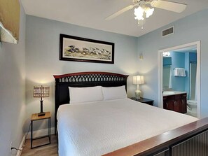 A bedroom with a bed, a nightstand, a lamp, a ceiling fan, and a framed picture on the wall.