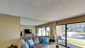 Ein modernes Wohnzimmer mit einem grauen Sofa, einem runden Couchtisch und einem großen Fenster mit Blick auf ein Gebäude und einen Brunnen.
