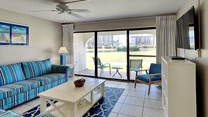 Una habitación de hotel moderna con un ventanal grande, ventilador de techo, sofá, mesa y televisor.