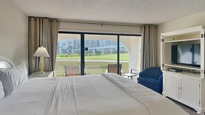 Ein Hotelzimmer mit einem großen Bett, einem Fernseher, einem Schreibtisch und Blick auf einen Golfplatz sowie Gebäude.
