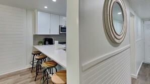A modern kitchen with white cabinets, a central island with stools, and a decorative mirror on the wall. - Edgewater Villa #505 | 11 Pools, Golf Course, & More (Panama City Beach)
