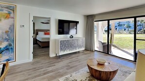 A modern hotel room with a large window, a flat-screen TV, a wooden coffee table, and a painting on the wall. - Edgewater Villa #505 | 11 Pools, Golf Course, & More (Panama City Beach)