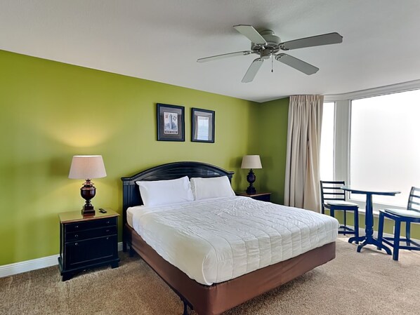A hotel room with a large bed, two bedside tables with lamps, a ceiling fan, and a view of the outdoors through a window.