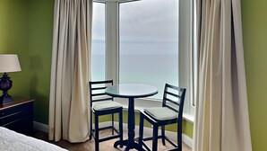 A hotel room with a corner table and two chairs, a lamp, and a view of the ocean through large windows. - Emerald Beach #1825 | Dining, Pool, Gym, & More! (Panama City Beach)