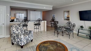 Una sala moderna con un sofá estampado, un comedor con mesa de vidrio, y una cocina al fondo.