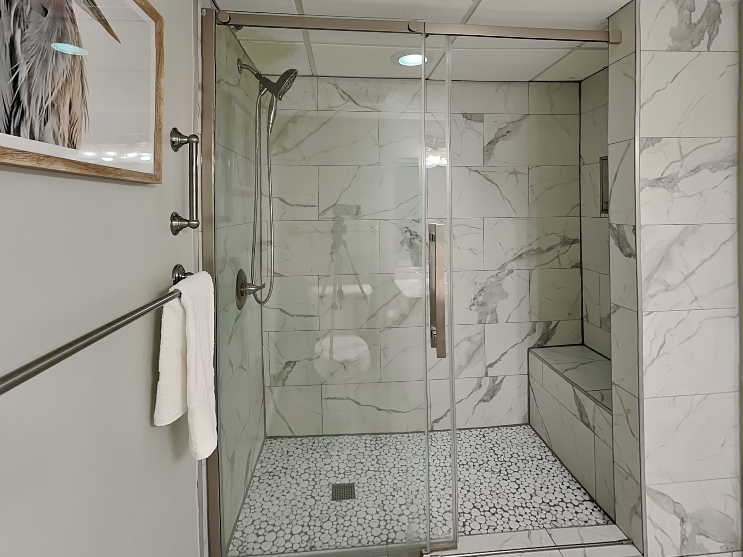 Una ducha moderna con puerta de vidrio, azulejos de mármol y suelo con diseño de guijarros.