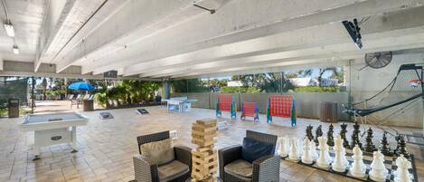 Un patio al aire libre con mobiliario de mimbre, una mesa de fútbol de mesa y un ajedrez grande.