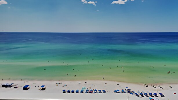 A beach with clear turquoise waters, a sandy shore, and several beach umbrellas and lounge chairs. - Grandview East #1305 | Breathtaking views! (Panama City Beach)