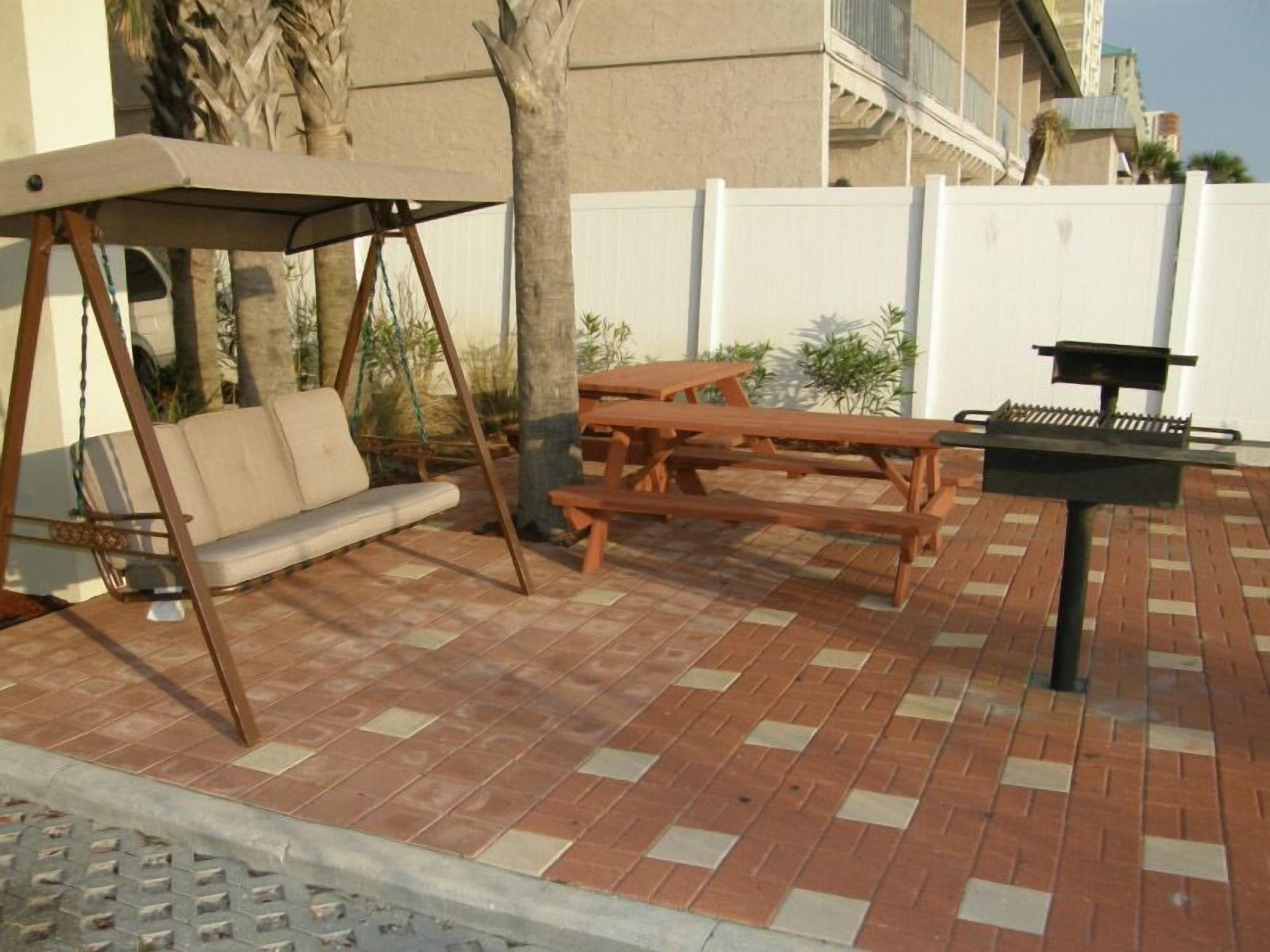 Un patio al aire libre con una hamaca, un banco de madera y una parrilla.