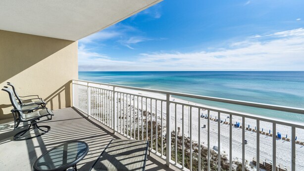 A balcony with a view of the beach, a table, and two chairs.