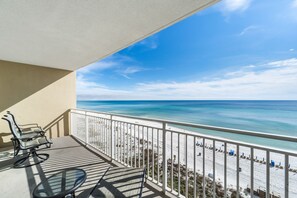 A balcony with a view of the beach, a table, and two chairs. - Emerald Beach #728 | Incredible Amenities & Views! (Panama City Beach)