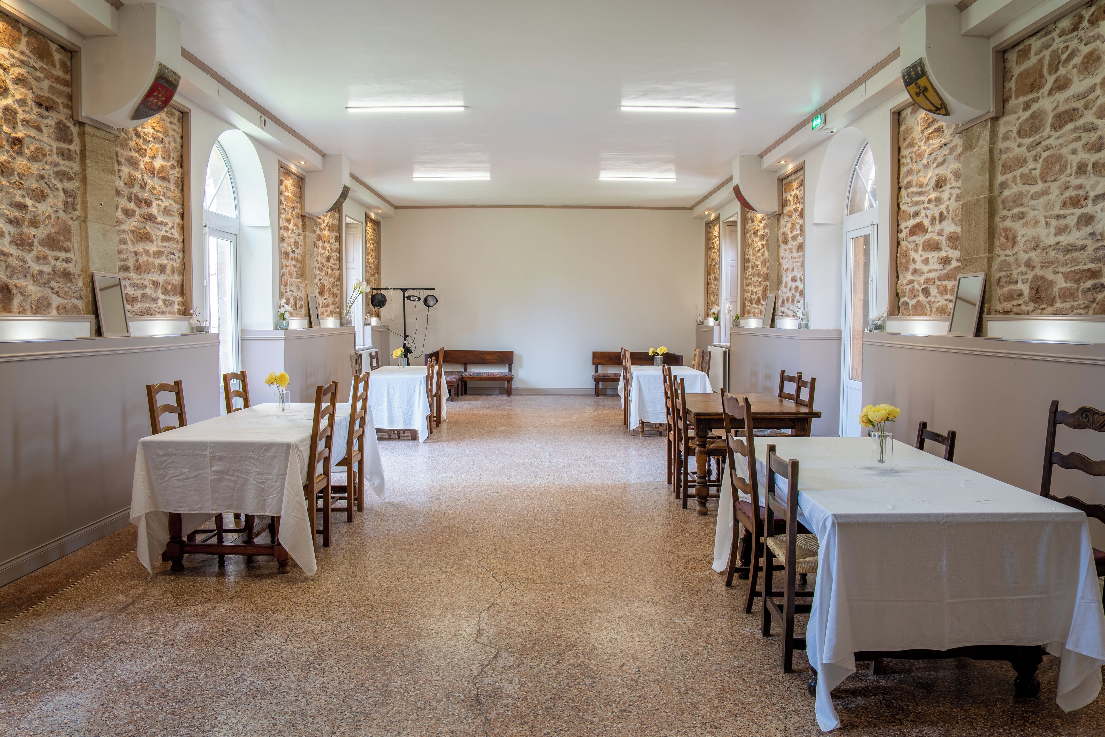 Une vaste salle à manger aux murs de pierre, dotée de nombreuses tables et de chaises.