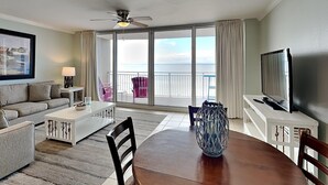 Hotelkamer met balkon, plafondventilator, televisie, eettafel met stoelen, bank en salontafel.