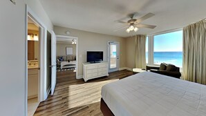 Ein Hotelzimmer mit Bett, Fernseher, Deckenventilator, Meerblick und einem Badezimmer mit Spiegel und Waschbecken.