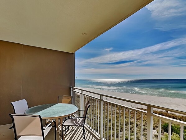A balcony with a table and chairs, overlooking a beach with a clear sky. - Emerald Beach #335 | 3 Pools, Gym, Dining! (Panama City Beach)