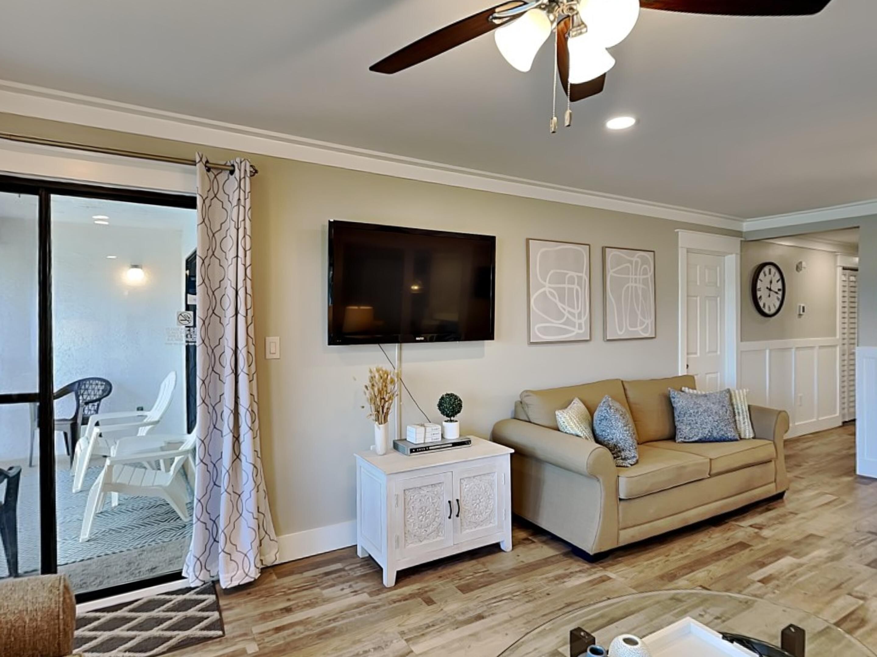 Un salon avec un canapé beige, un buffet blanc, un téléviseur à écran plat et un ventilateur de plafond.