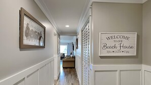 A hallway with a framed picture and a welcome sign to the beach house. - Edgewater Villa #909| Full-service resort! (Panama City Beach)