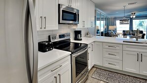 A modern kitchen with white cabinets, stainless steel appliances, and a built-in microwave. - Edgewater Villa #909| Full-service resort! (Panama City Beach)