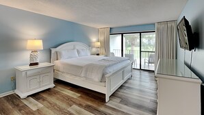 Un dormitorio con cama, mesitas de noche, televisor y balcón con cortinas.