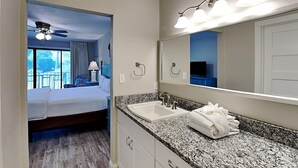 A hotel room with a bed, a bathroom with a sink and mirror, and a view of the outdoors. - Edgewater Villa #708 | Full-service resort! (Panama City Beach)