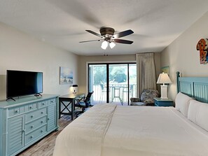 Une chambre d’hôtel équipée d’un lit, d’une télévision, d’un bureau, d’une chaise, d’un ventilateur de plafond et d’un balcon avec des chaises.